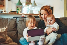 Eine Mutter sitzt mit ihren zwei kleinen Kindern auf dem Sofa und bedient ein Tablet.