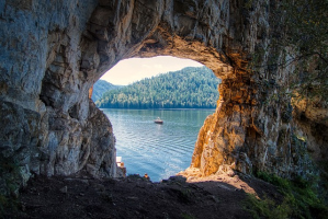 Blick durch ein natürliches Felsfenster auf einen See mit einem Boot für trip´dip Entdecker.