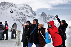 Eine Reisegruppe macht ein Selfie mit einem Selfie-Stick in einer verschneiten Berglandschaft für trip´dip.